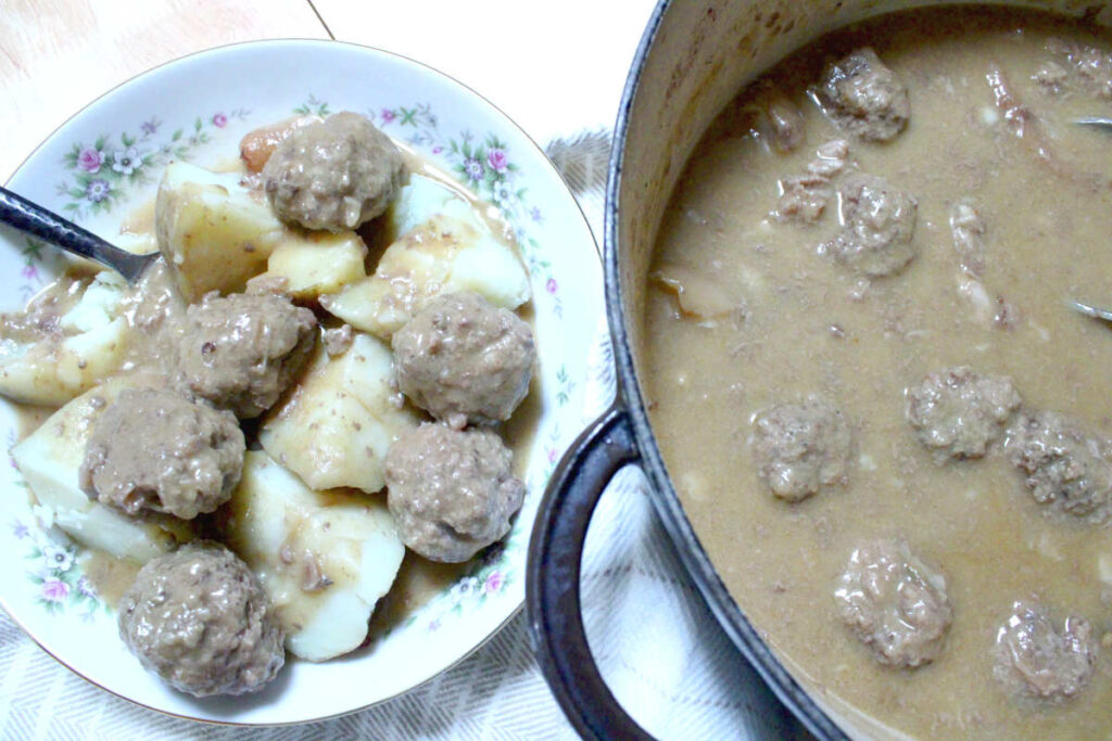 pork hock and meatball stew - potatoes and meatballs covered with gravy in a bowl and the remaining stew to the right in the pot