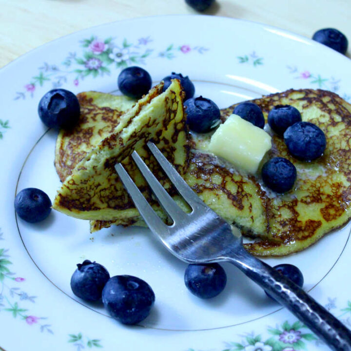 banana egg pancakes on a plate covered with blueberries and butter with a piece cut out on a fork