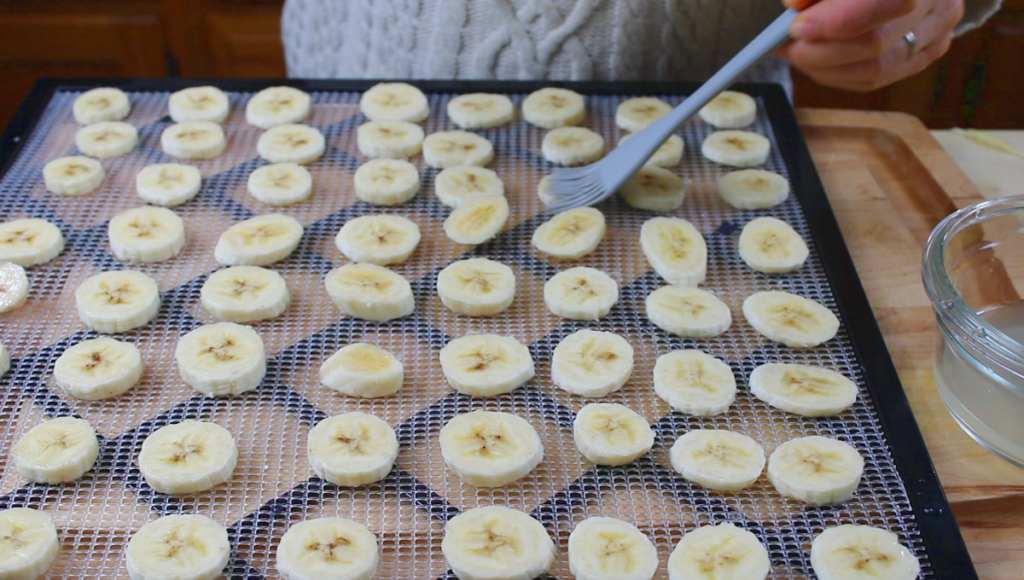 freshly sliced bananas on dehydrator tray applying the lemon juice mixture
