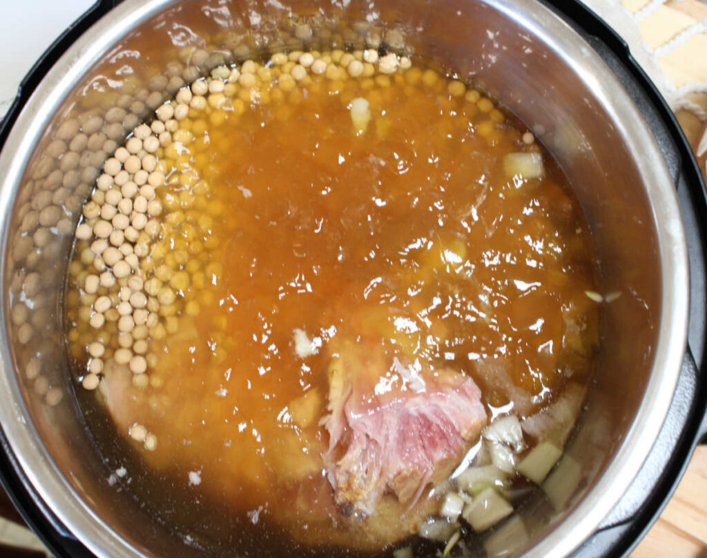 slow cooker ham and pea soup - a pan filled with onions, ham bone and chunks and bone broth/meat stock