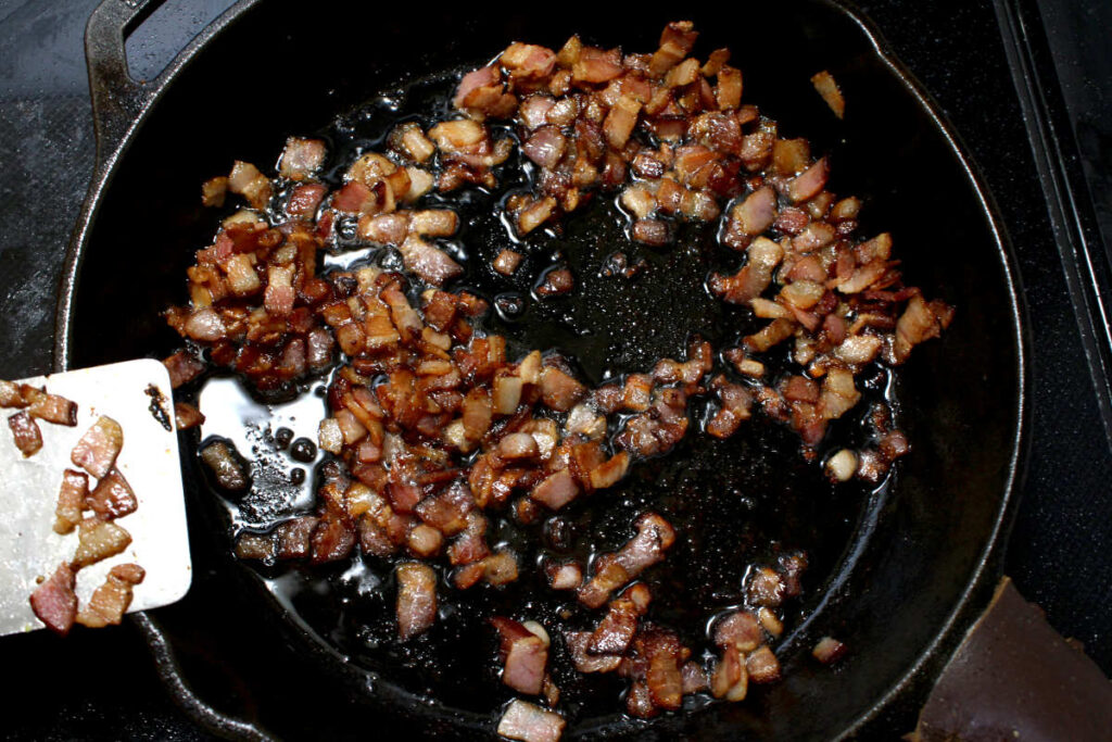 bacon bits cooking in a cast iron pan on stove