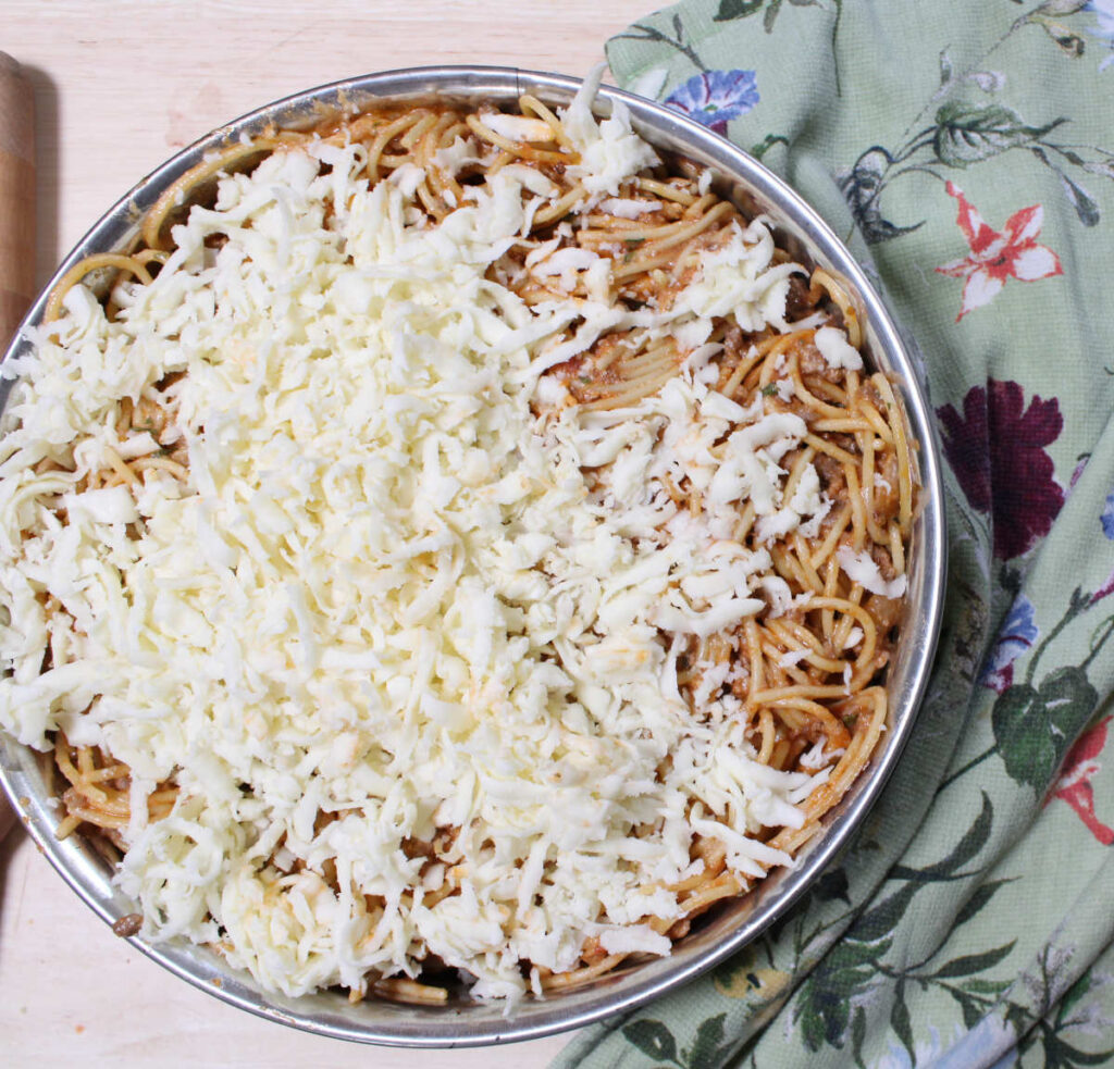spaghetti pie ingredients put in a springform pan and covered with shredded cheese